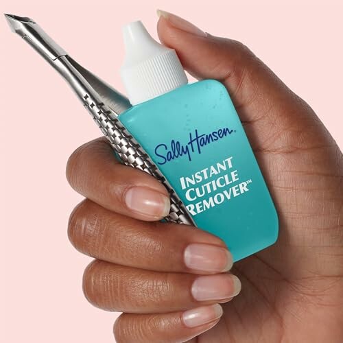 Hand holding Sally Hansen Instant Cuticle Remover and metal tool.