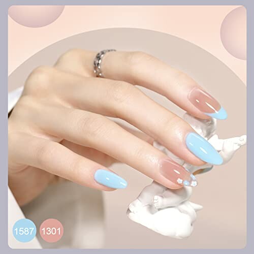 Hand with pastel blue and clear nail art holding a small white statue.